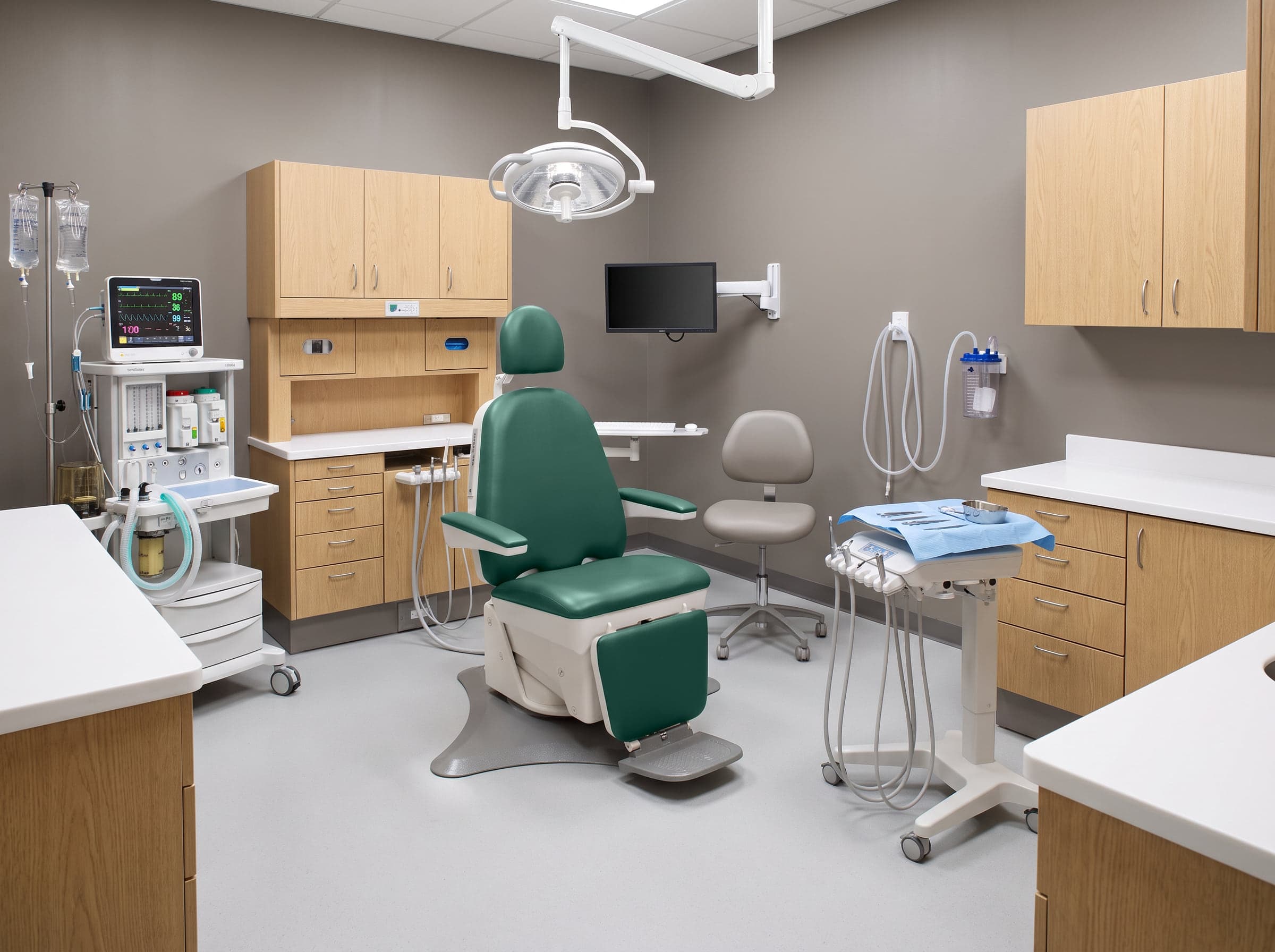 A generated surgical operatory around a Boyd chair: cabinetry, a surgical light, a monitor arm, an anesthesia cart and a patient monitor