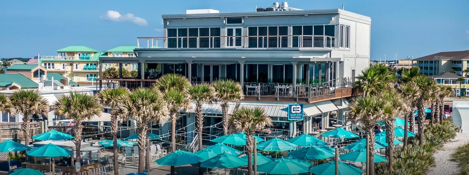 The Casino Beach Bar & Grille building on Pensacola Beach, the CB sign above a patio of teal umbrellas