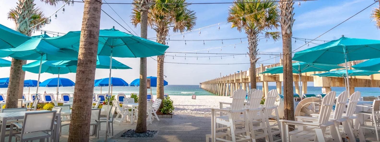 The beachfront patio: teal umbrellas and white chairs looking out to the Gulf and the pier