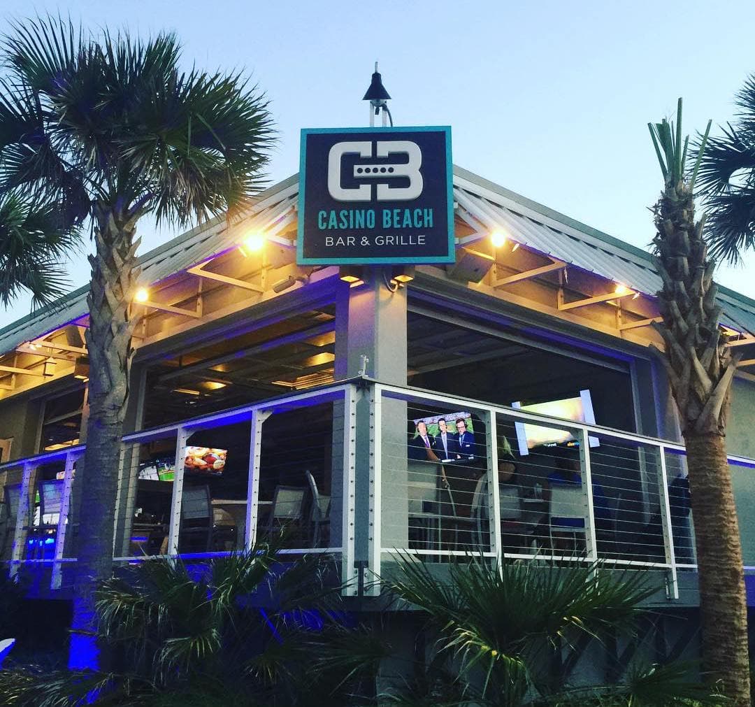 The illuminated Casino Beach Bar & Grille sign on the building at dusk, framed by palms