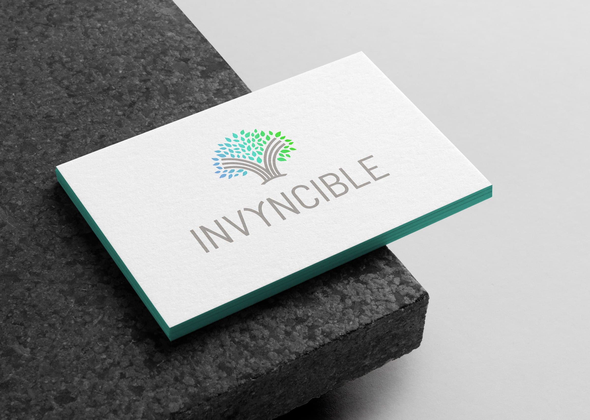 Invyncible business card with a teal edge, resting on a dark textured surface