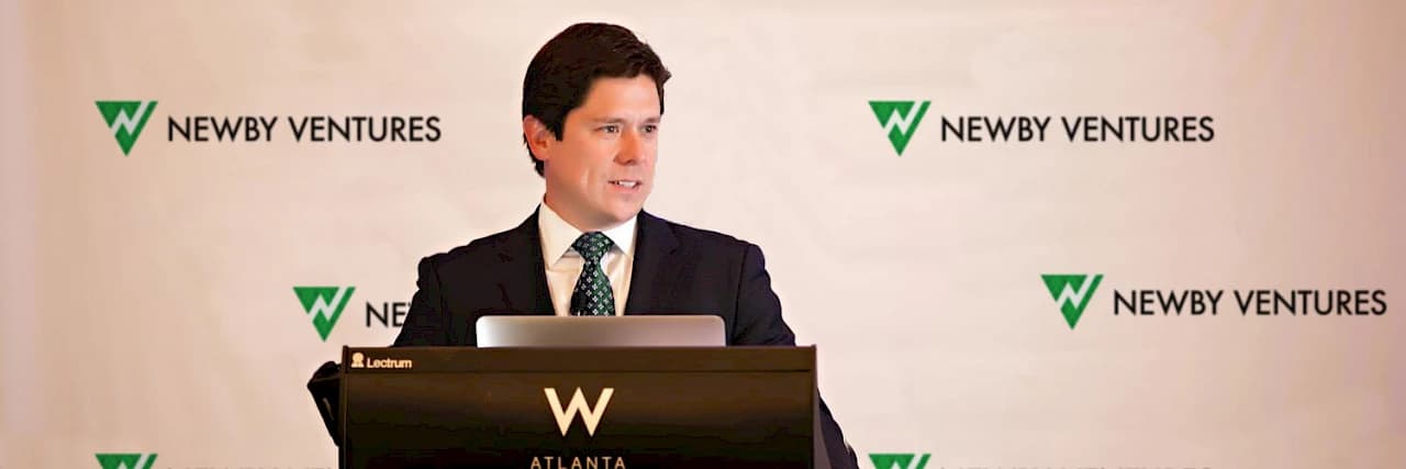 Hunter Newby speaking at a podium in front of a Newby Ventures branded backdrop at the W Atlanta