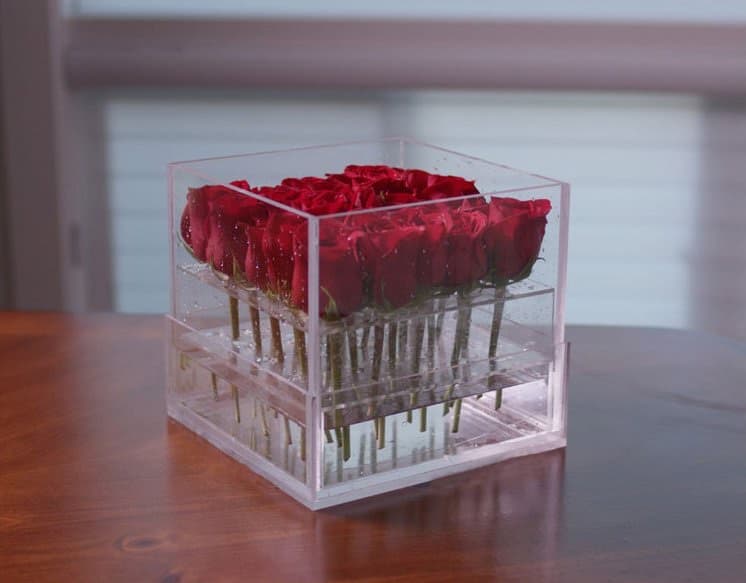 A Tulu arrangement of red roses in a clear acrylic keepsake box on a table